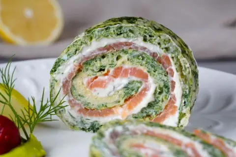 Ein saftiger Spinat Lachs Rolle auf einem Teller, garniert mit Dill und Zitrone.