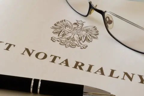 Okulary i długopis leżą na dokumencie z godłem Polski i napisem "AKT NOTARIALNY". To dokument, który wymaga opłaty, czyli taksa notarialna.