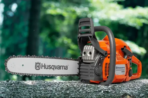 Pomarańczowa piła łańcuchowa Husqvarna 445 na pniu drzewa. Sprawdź husqvarna 445 dane techniczne, by poznać jej możliwości.
