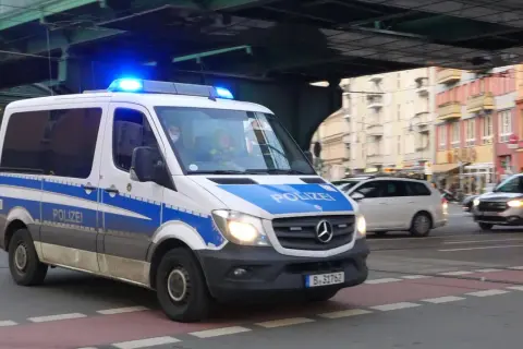 Polizeivan mit Blaulicht fährt auf der Straße. Ein polizeiliches Verkehrszeichen ist auf dem Fahrzeug angebracht.