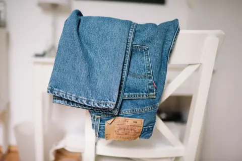 Złożone, klasyczne jeansy Levi Strauss wiszą na białym krześle. Widoczna metka z logo marki.