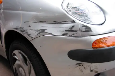 Uszkodzony srebrny błotnik i zderzak auta z widocznymi śladami po otarciu. Jak usunąć rysy z auta?