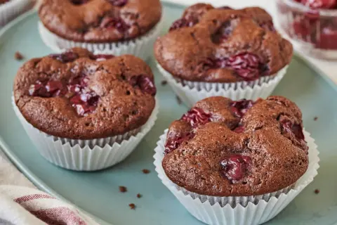 Schoko Kirsch Muffins auf einem blauen Teller, mit Kirschen garniert. Ein Genuss für jeden Schokoladenliebhaber.