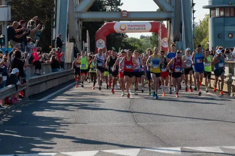 Coureurs au départ du semi-marathon Paris 2026, sous une arche Harmonie Mutuelle. Le soleil brille, les spectateurs encouragent.