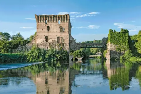 Rovine di un castello e un ponte sul Mincio, con riflessi sull'acqua calma.