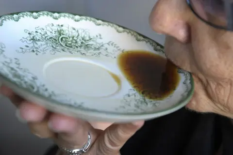 En person dricker gammalt kaffe direkt ur en tefat med grön dekor.