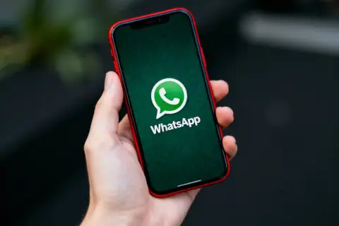 Dłoń trzyma iPhone'a z logo WhatsApp. Dowiedz się, jak przenieść czaty WhatsApp z Androida na iPhone.
