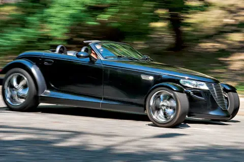 Czarny Plymouth Prowler z opuszczonym dachem pędzi po krętej drodze, otoczony rozmazaną zielenią drzew.