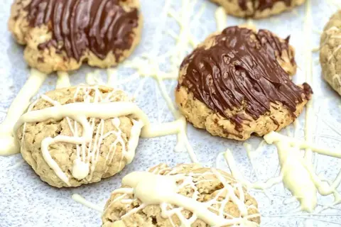 Leckere Haferflocken Kekse, einige mit Schokoladenglasur, andere mit weißer Schokolade verziert, auf einem hellen Untergrund.