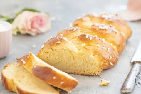 Ein goldbrauner Hefezopf, bestreut mit Hagelzucker, liegt angeschnitten auf grauem Untergrund. Ein tolles Rezept für Hefezopf!