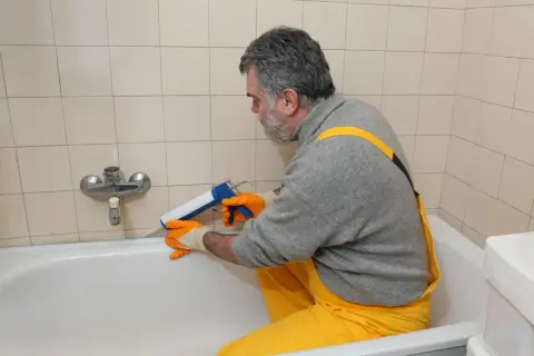 Mann erneuert mit Kartuschenpresse die silikonfugen an der Badewanne.