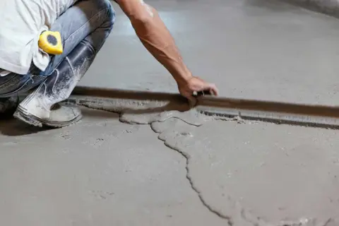 Obrero usa regla para nivelar suelo de cemento fresco.
