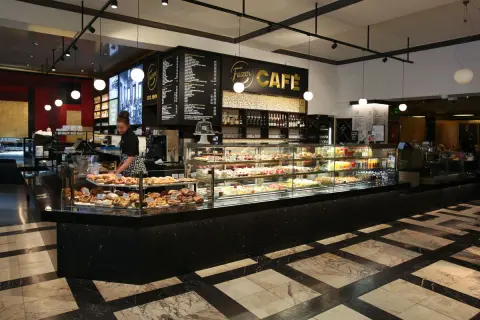 En kvinna arbetar bakom disken på Fazer Café i Helsingfors. Disken är fylld med bakverk och tårtor.