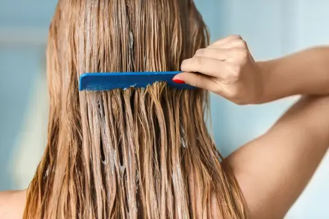 Une main peigne des cheveux blonds humides, recouverts d'un masque argile avant coloration végétale.