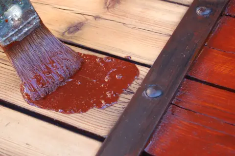 Pinceau appliquant une peinture marron sur des volets en bois sans décaper.