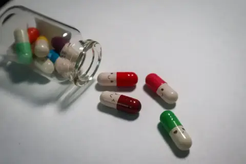 Kolorowe kapsułki, niektóre z uśmiechniętymi buźkami, wypadają z buteleczki. To mogą być psychotropy, które pomagają w trudnych chwilach.