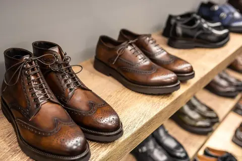 Vari tipi di scarpe eleganti in pelle marrone e nera, con dettagli traforati, disposte su scaffali di legno.