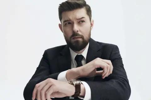 Mężczyzna w garniturze, z zarostem, zastanawia się, czy Remigiusz Mróz ma żonę.