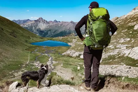 Un randonneur et son chien contemplent un lac bleu et des montagnes majestueuses. Une belle randonnée avec chien.