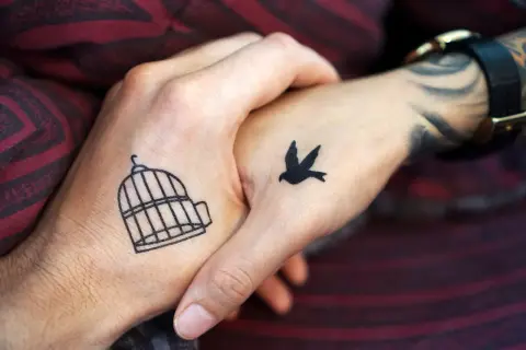 Zwei Hände mit leichten Tattoos zum selber zeichnen: Ein Vogel fliegt aus einem Käfig.