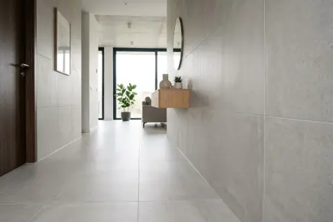 Pasillo moderno con paredes y suelo cubiertos de azulejos en horizontal o vertical. Una puerta de madera oscura a la izquierda y un mueble flotante con decoración a la derecha.