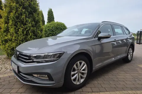 Szary Volkswagen Passat Variant z polskimi tablicami rejestracyjnymi stoi na podjeździe z kostki brukowej, otoczony zielenią.