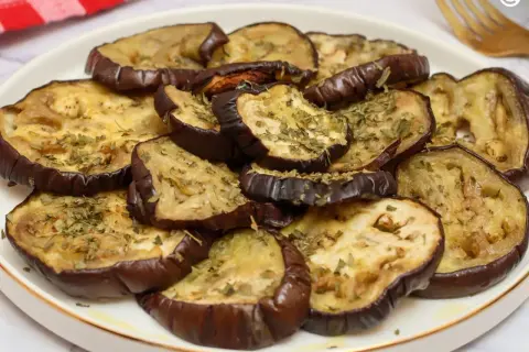 Rodajas de berenjenas asadas al horno, tiernas y doradas, espolvoreadas con hierbas aromáticas.