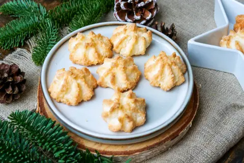 Leckere Kokosmakronen, die nach einem einfachen Rezept gelingen. Perfekt für die Weihnachtszeit, umgeben von Tannenzweigen und Zapfen.