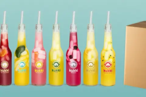 Reihe von Kukki Cocktails in Flaschen mit Früchten und Eis, daneben eine Pappbox.