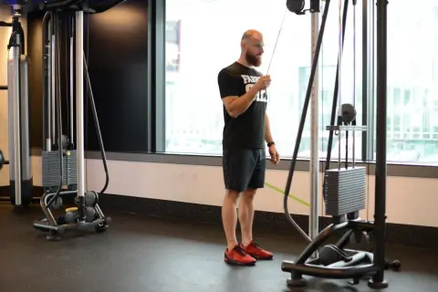 Mężczyzna wykonuje prostowanie ramion na wyciągu, ćwicząc triceps.
