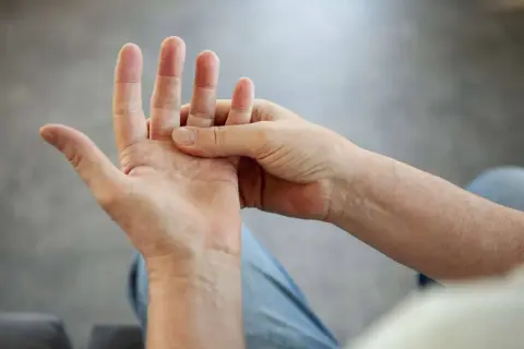 Person massiert Hand, da die Finger schmerzen beim Beugen.