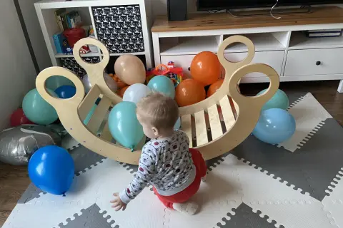 Roczne dziecko bawi się z kolorowymi balonami przy drewnianej kołysce. To idealne miejsce do rozwoju metodą Montessori.