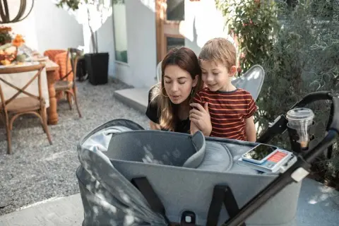 Mama i synek pochylają się nad gondolą spacerówki, jakby zastanawiali się, od kiedy spacerówka będzie im potrzebna.