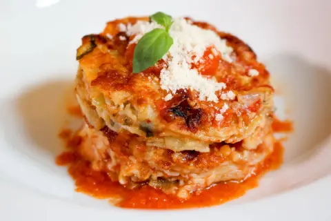 Parmigiana di alici, un tortino stratificato con pesce, verdure e pomodoro, guarnito con basilico e parmigiano.
