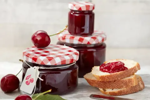 Gläser mit kirsch marmelade, frische Kirschen und Brot mit Marmelade.