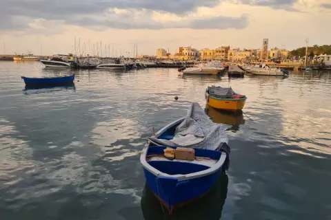 Barche nel porto al tramonto, con la città sullo sfondo. Un'atmosfera di pace e contemplazione, quasi un soffio di **santo spirito** sul mare calmo.