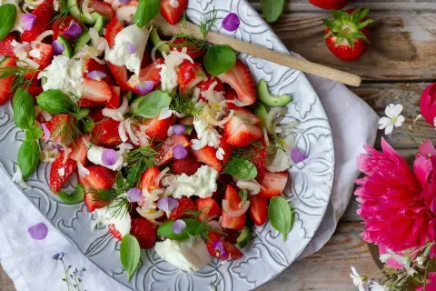 En härlig somrig sallad med jordgubbar, mozzarella, gurka och färska örter, dekorerad med ätbara blommor.