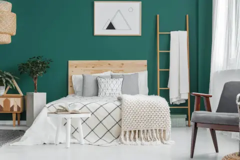 Chambre parentale cosy aux murs vert émeraude, lit en bois, plaids douillets et plantes vertes pour une ambiance relaxante.