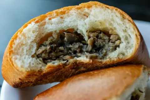 Puszysta bułka z pieczarkami, przekrojona na pół, odsłaniająca aromatyczne, drobno posiekane grzyby. Idealna na szybką przekąskę.