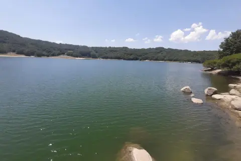 Un lago sereno rodeado de colinas verdes, con rocas en la orilla. Un lugar perfecto para desconectar en Xares a Veiga.