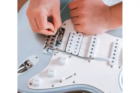 Ręce montują nową strunę do mostka gitary elektrycznej. Praktyczny poradnik, jak zmienić struny w gitarze elektrycznej.