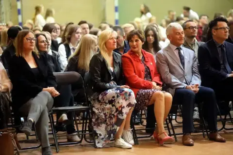 Uczestnicy sali, w tym nauczyciele, siedzą w pierwszym rzędzie, słuchając uważnie. To ważna rada pedagogiczna.