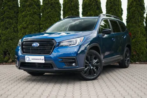 Błękitny Subaru Ascent z czarnymi felgami stoi przed żywopłotem.