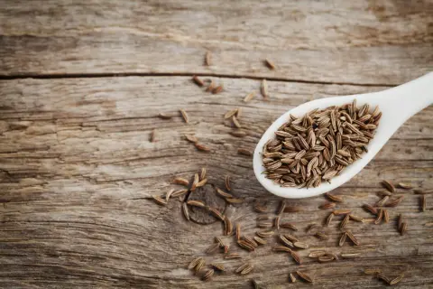 Ein Löffel voller Kreuzkümmelsamen, die für ihre verdauungsfördernde cumin wirkung bekannt sind, liegen auf rustikalem Holz.
