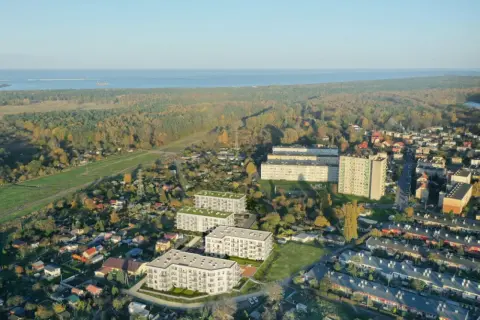 Nowoczesne bloki mieszkalne wyrastają pośród zieleni i domów jednorodzinnych, tworząc nowe młode stogi w krajobrazie. W tle morze i jesienny las.