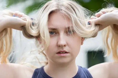 Blondes Haar, das mit Kamillentee behandelt wurde, zeigt vorher-nachher-Effekte. Die Frau hält ihre blonden Zöpfe hoch.