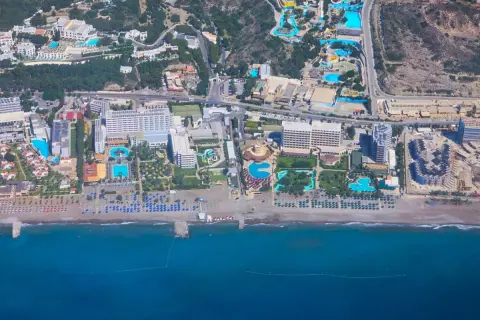 Vy från ovan över ett stort vattenland och hotellkomplex vid Rhodos kust. Solstolar och parasoller kantar stranden.