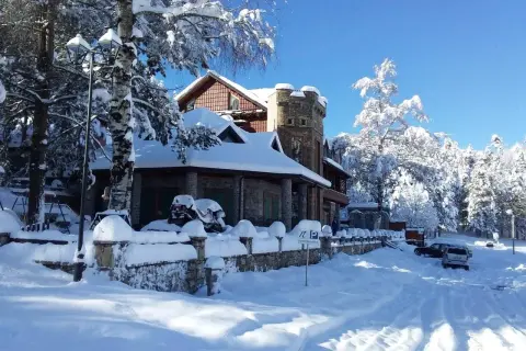 Un hermoso paisaje de Albania en invierno, con una casa cubierta de nieve y árboles nevados bajo un cielo azul brillante.