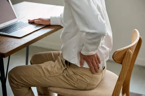 Homme assis à un bureau, se tenant le bas du dos. Il se demande combien de temps d'arrêt pour une discopathie.