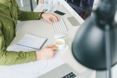 Pracownik biurowy z kawą analizuje wykresy. Czy działalność gospodarczą w domu trzeba zgłaszać?
